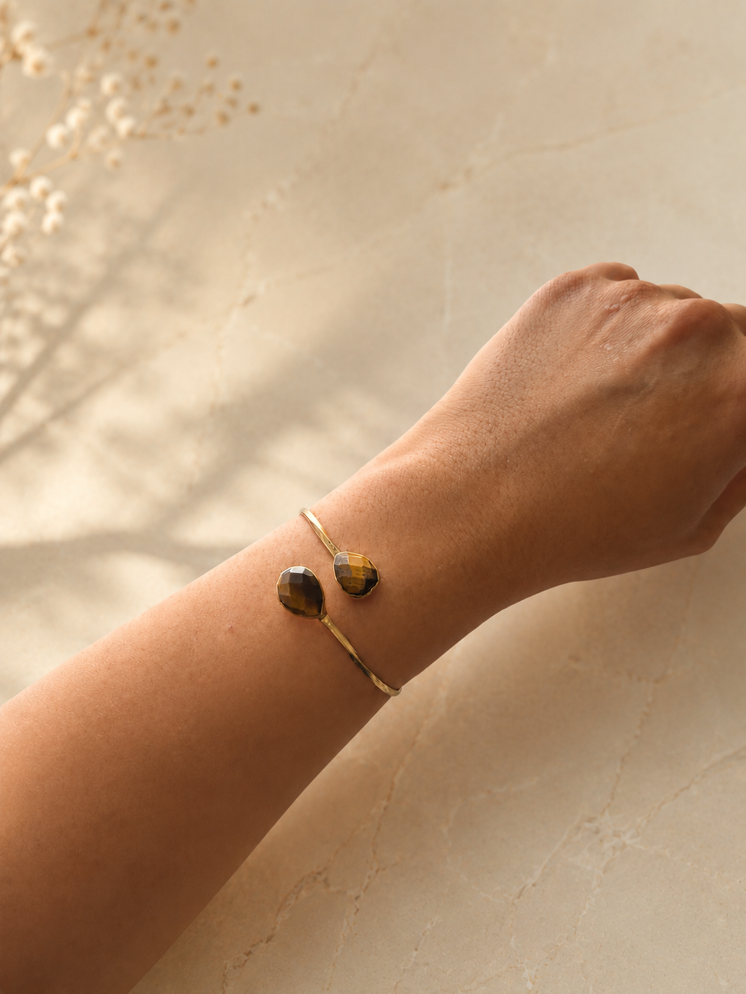 Zivèra handgemaakte tijgeroog dubbelsteen armband 18K goldplated aan pols met droogbloemen op beige achtergrond